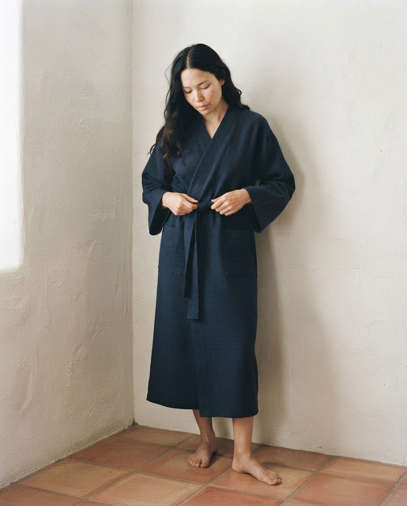 Femme nouant la ceinture d'un peignoir long nid d'abeille bleu marine, regard baissé