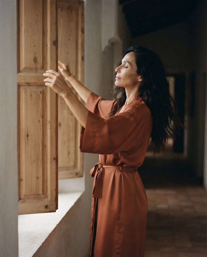 Femme en peignoir satin terracotta ouvrant un volet, manches kimono trois-quarts