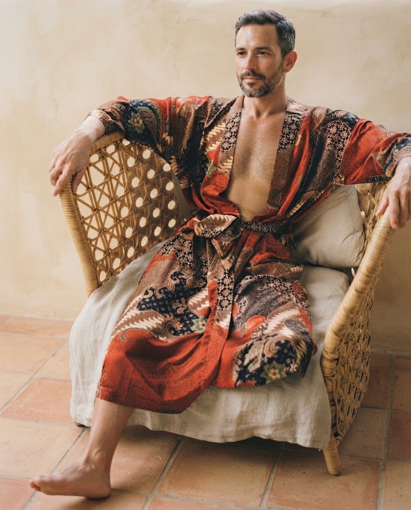 Homme assis dans un fauteuil en rotin, vêtu d'un peignoir kimono en satin imprimé rouille à motifs cachemire