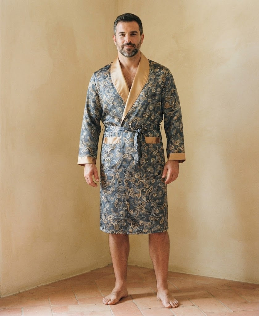 Homme debout pieds nus portant une robe de chambre en satin paisley bleu ardoise à col châle doré, dans une pièce aux murs ocre